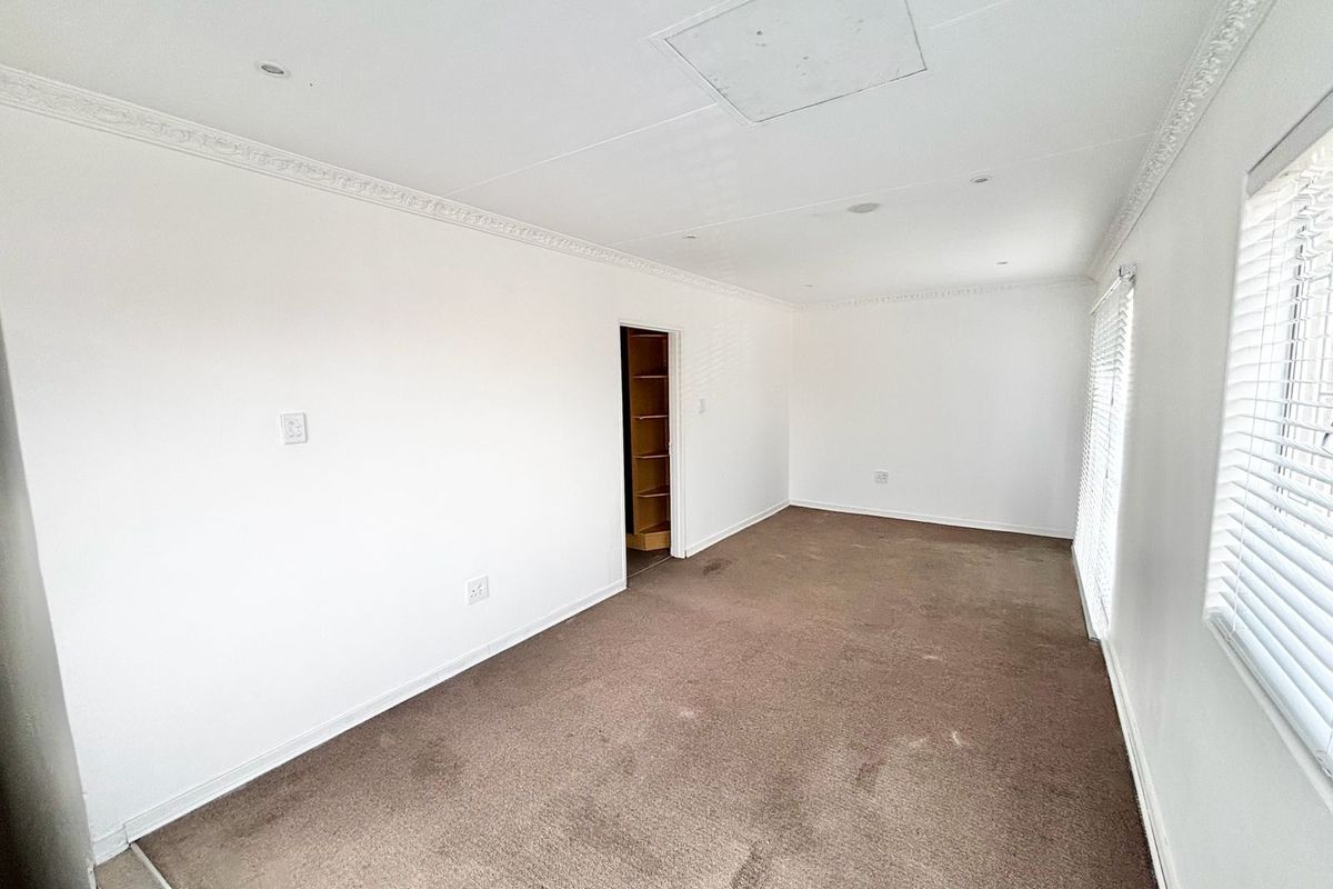 A spacious, empty bedroom featuring neutral walls, crown molding, fitted carpet, and built-in shelving visible through the doorway.