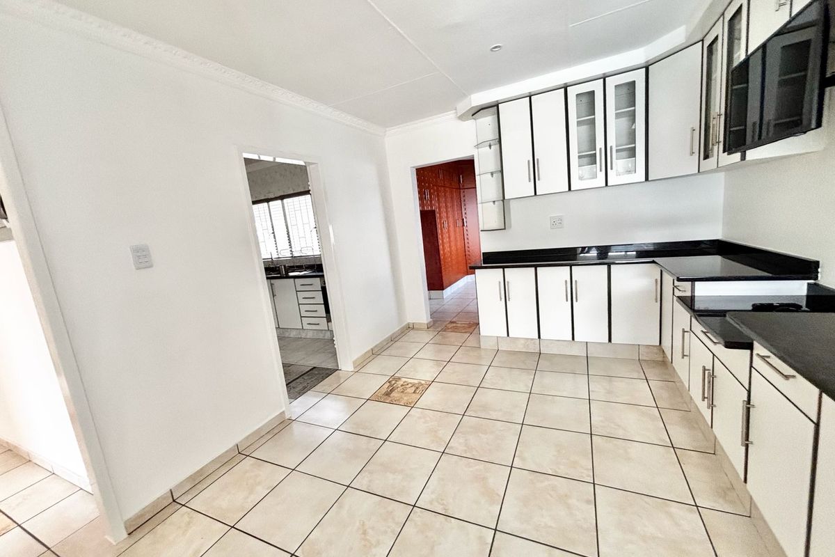 A functional kitchen featuring white cabinetry, black countertops, and tiled flooring, with an adjacent scullery area visible through the doorway.