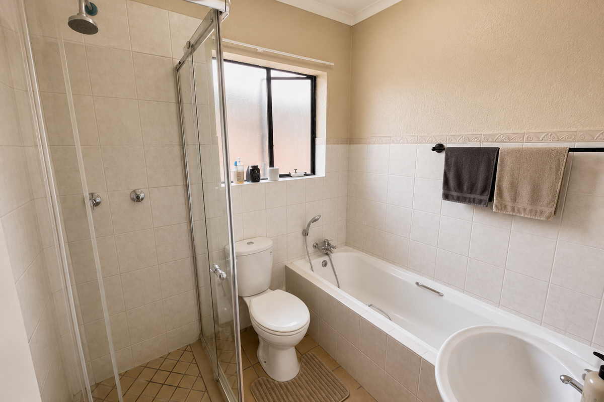 A functional bathroom featuring a separate shower enclosure, a bathtub with handheld shower attachment, a toilet, and neutral wall tiling.