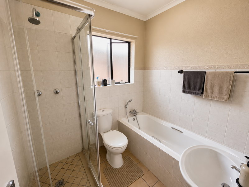A functional bathroom featuring a separate shower enclosure, a bathtub with handheld shower attachment, a toilet, and neutral wall tiling.