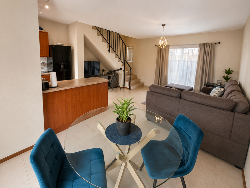 An open-plan living and kitchen area featuring tiled floors, a breakfast counter, and a staircase with a metal balustrade leading to the upper level.