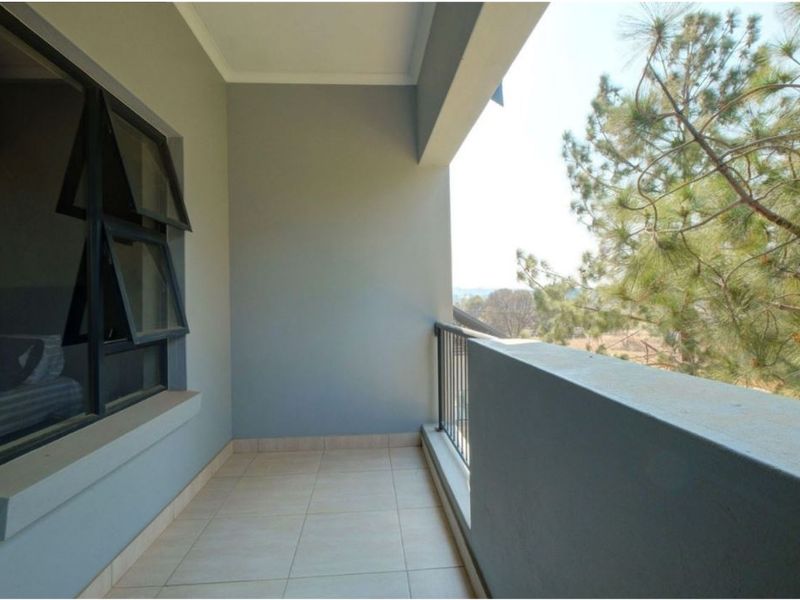 A clean, covered balcony featuring tiled flooring, a metal balustrade, and views of the surrounding trees.