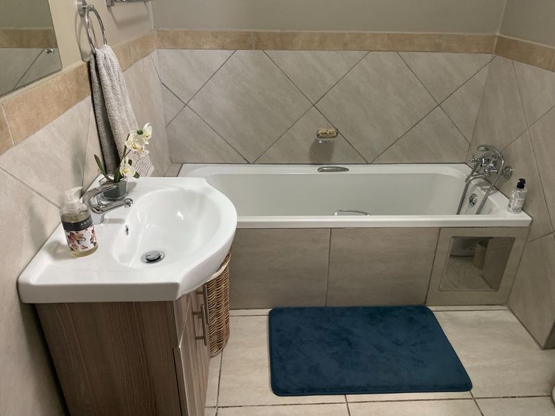 A well-maintained bathroom featuring a built-in bathtub, a modern vanity cabinet with a ceramic basin, and neutral-toned wall and floor tiling.