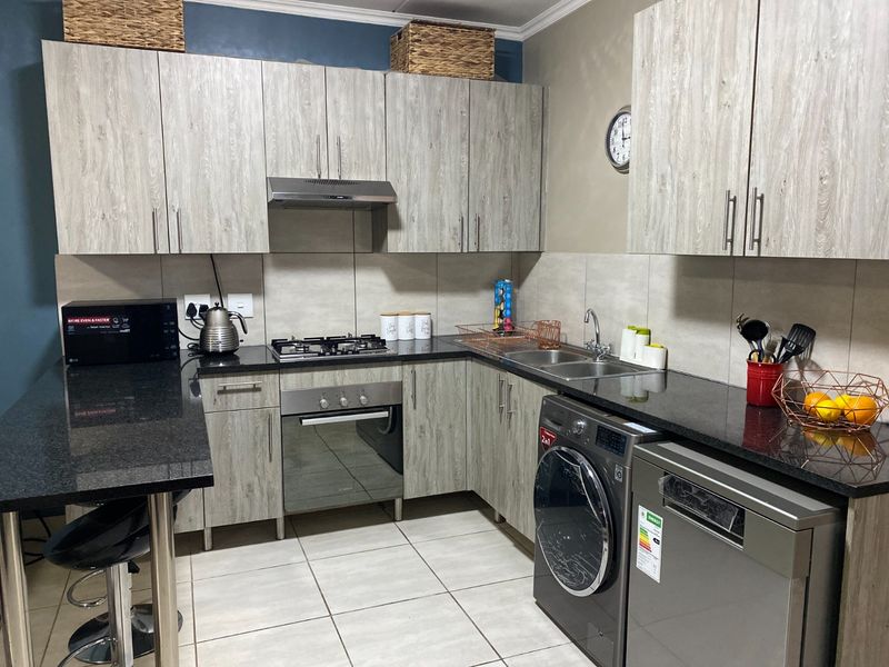 Modern kitchen featuring granite countertops, light wood-grain cabinetry, built-in oven with gas hob, extractor fan, and tiled finishes throughout.