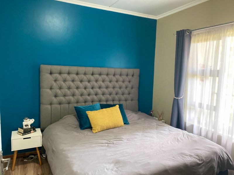 A bedroom featuring laminate flooring, crown molding, and a bold blue accent wall, providing a comfortable and well-defined sleeping space.