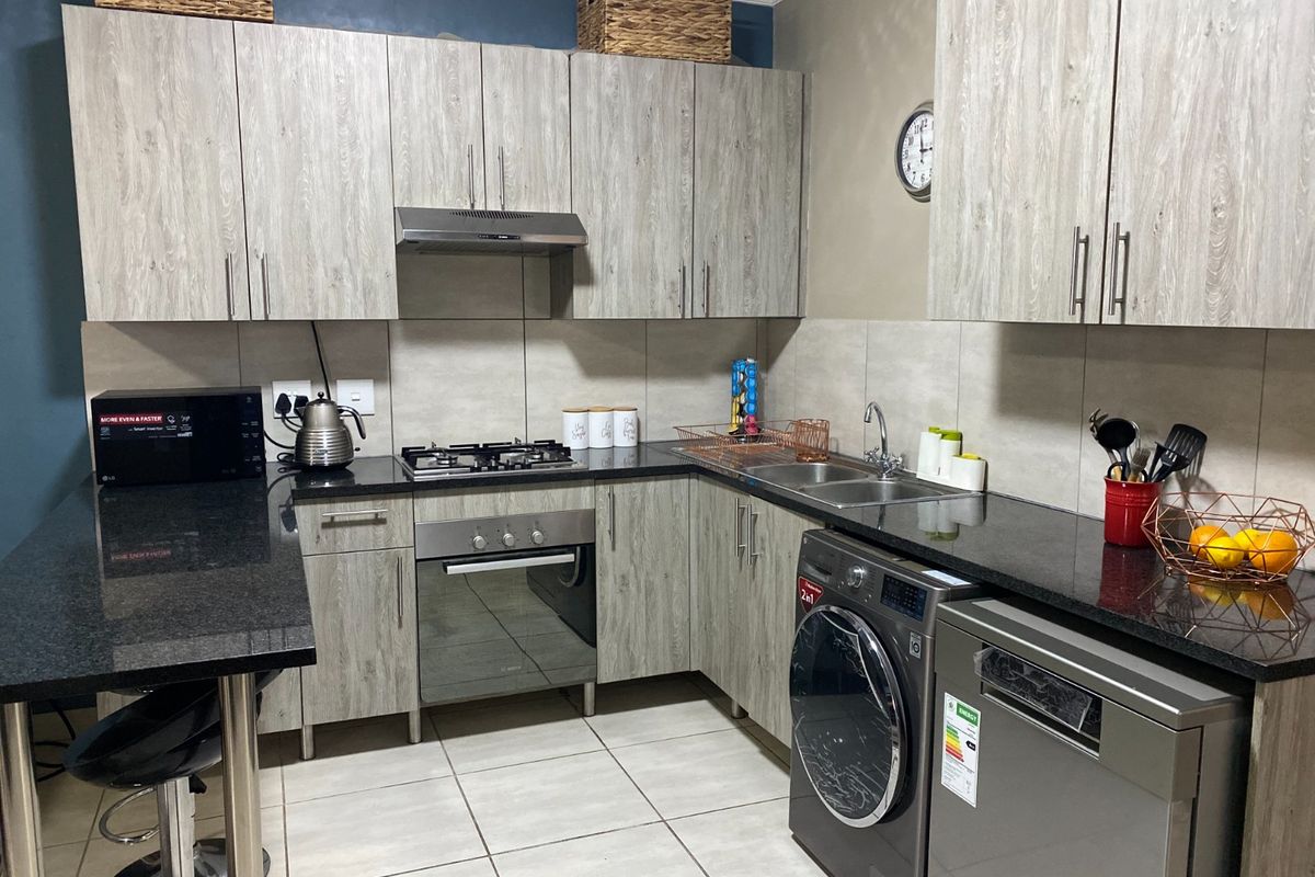 Modern kitchen featuring granite countertops, light wood-grain cabinetry, built-in oven with gas hob, extractor fan, and tiled finishes throughout.