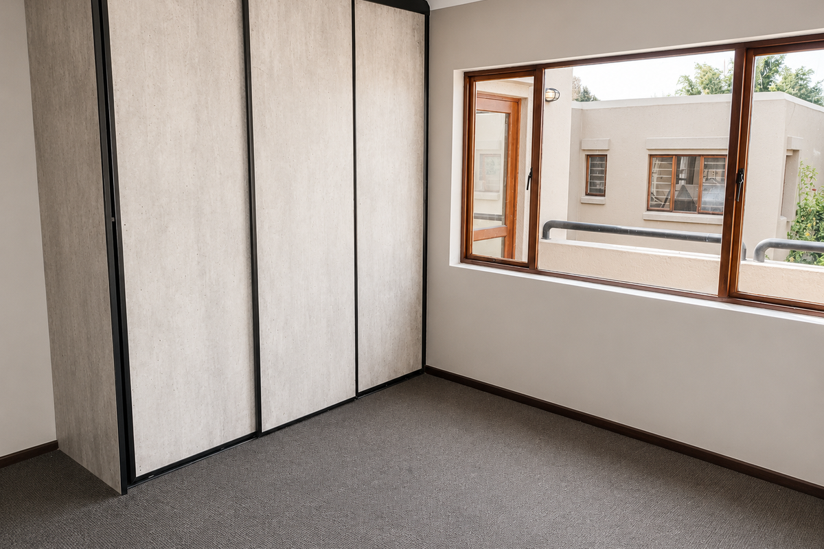 A bright, empty bedroom featuring neutral carpeted flooring and a large built-in wardrobe with modern sliding doors.