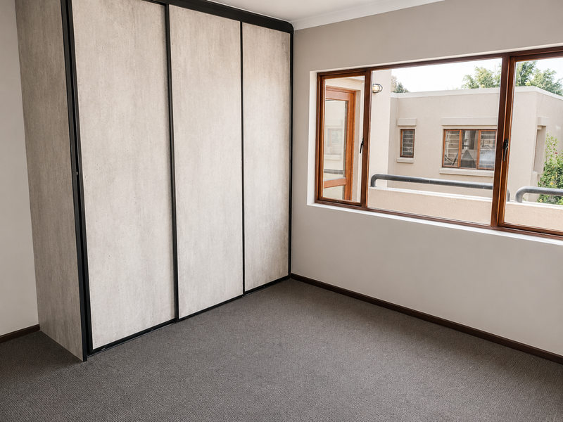 A bright, empty bedroom featuring neutral carpeted flooring and a large built-in wardrobe with modern sliding doors.