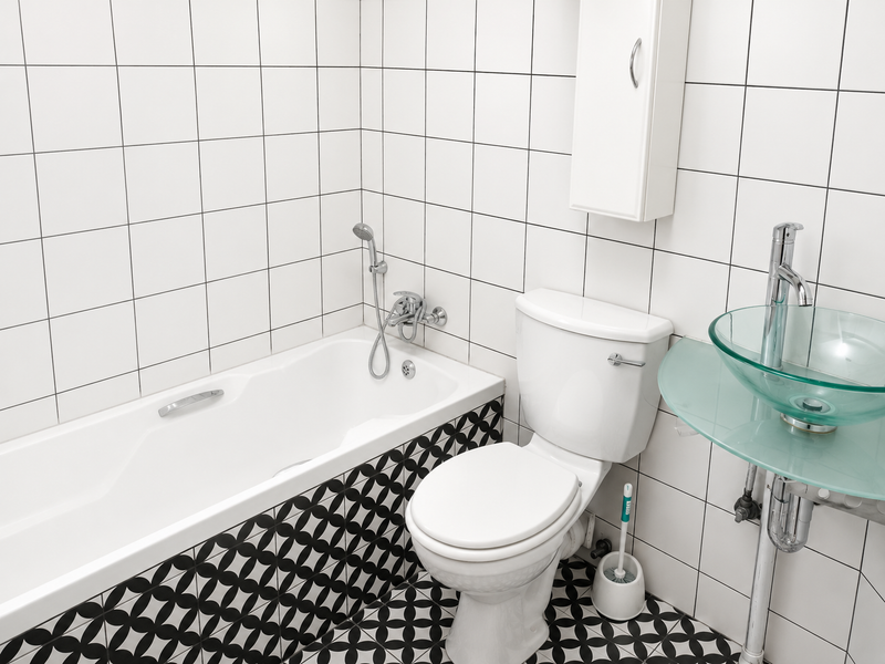 A modern bathroom featuring a bathtub with handheld shower, a white toilet, and a contemporary glass vessel sink with patterned floor tiling.