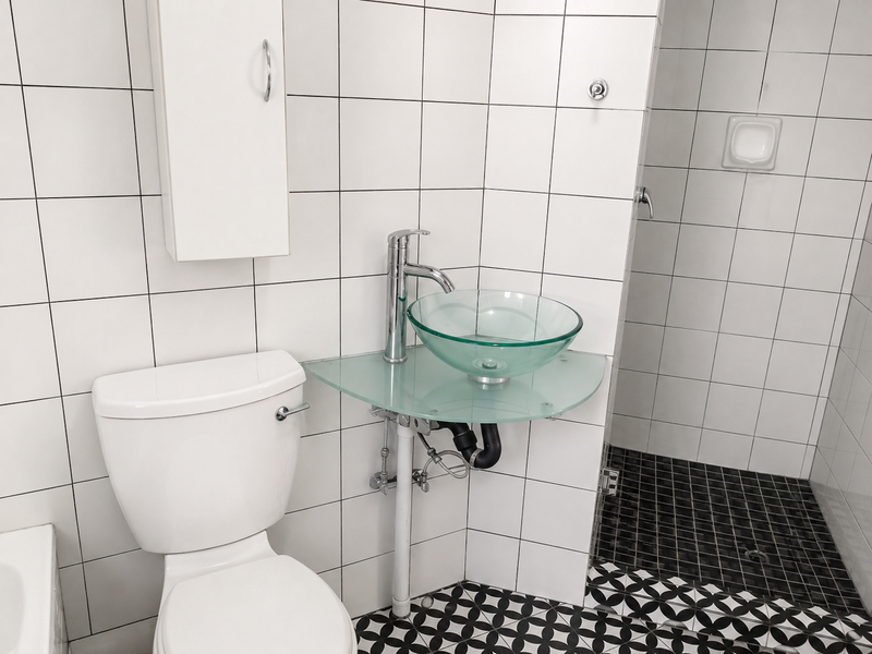 A clean, modern bathroom featuring a glass vessel sink, chrome fixtures, white wall tiles, and a distinct patterned floor.