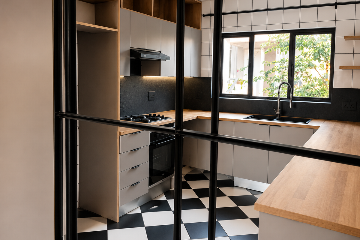 Modern kitchen featuring light grey cabinetry, wooden countertops, a gas hob, and a striking black and white checkered floor, viewed through a stylish metal divider.