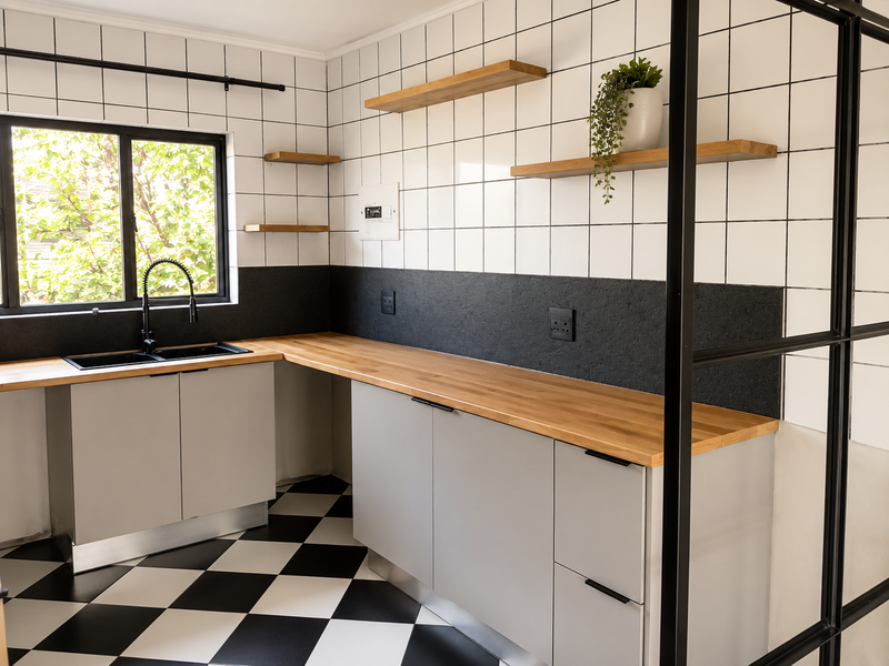 Modern kitchen featuring wooden countertops, black sink with gooseneck faucet, floating shelves, and distinctive black and white checkered flooring.
