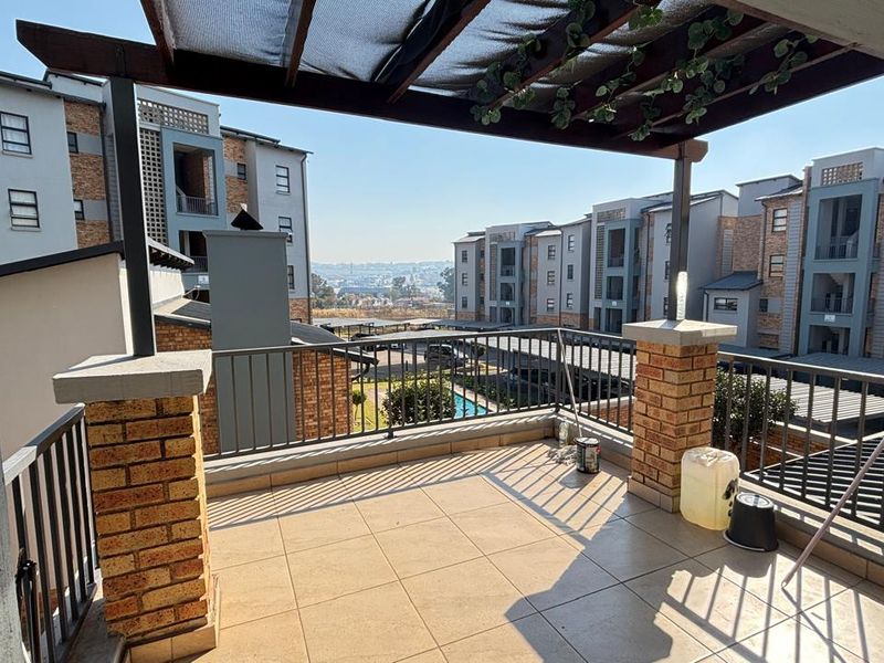 A spacious balcony featuring tiled flooring, brick pillars, and a timber pergola, offering an open view of the surrounding apartment complex.