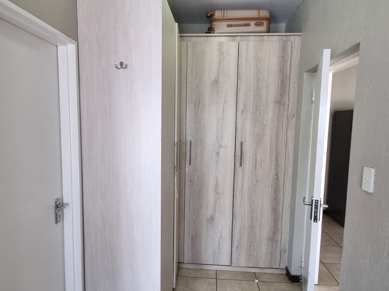 A functional hallway featuring light wood-finish built-in cupboards and tiled flooring, providing efficient storage and access to adjacent rooms.