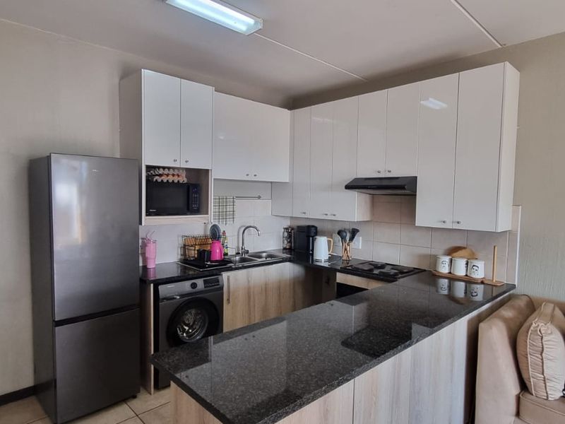 Compact open-plan kitchen featuring modern granite countertops, white cabinetry, and integrated appliances, seamlessly flowing into the adjacent living area.