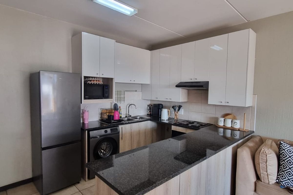 Compact open-plan kitchen featuring modern granite countertops, white cabinetry, and integrated appliances, seamlessly flowing into the adjacent living area.