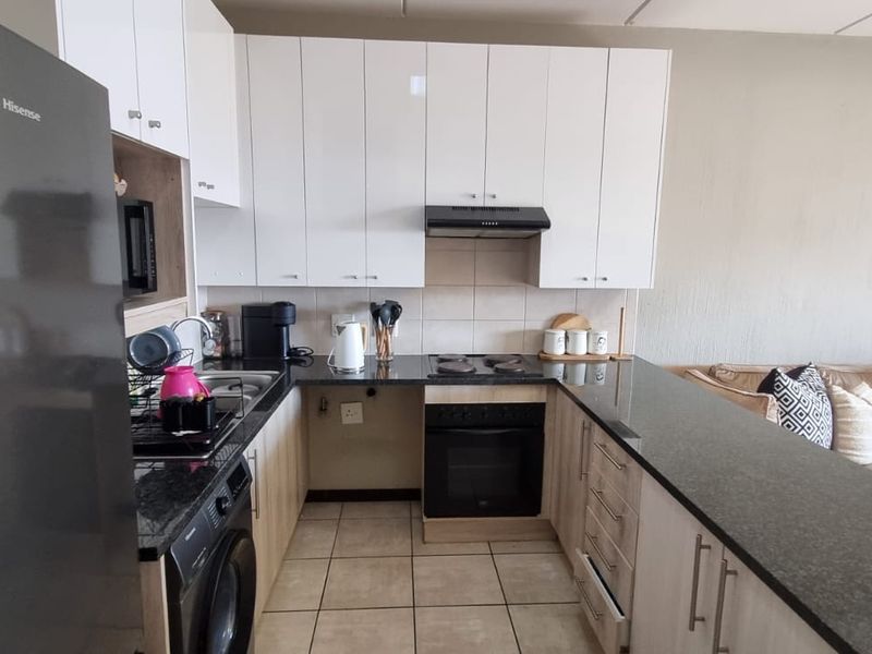 Open-plan kitchen featuring white cabinetry, granite countertops, built-in oven, hob, and extractor fan, seamlessly flowing into the adjacent living area.