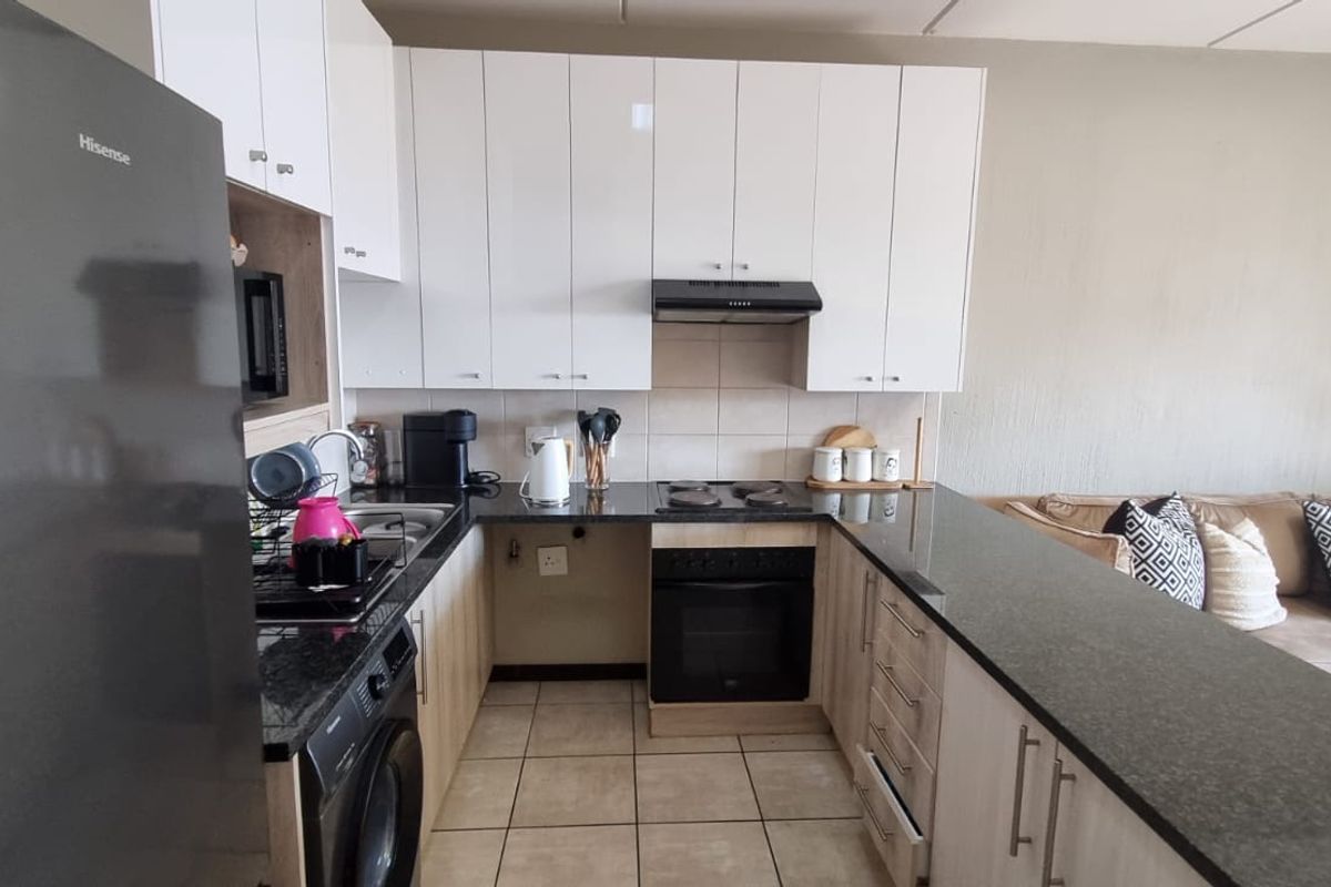Open-plan kitchen featuring white cabinetry, granite countertops, built-in oven, hob, and extractor fan, seamlessly flowing into the adjacent living area.