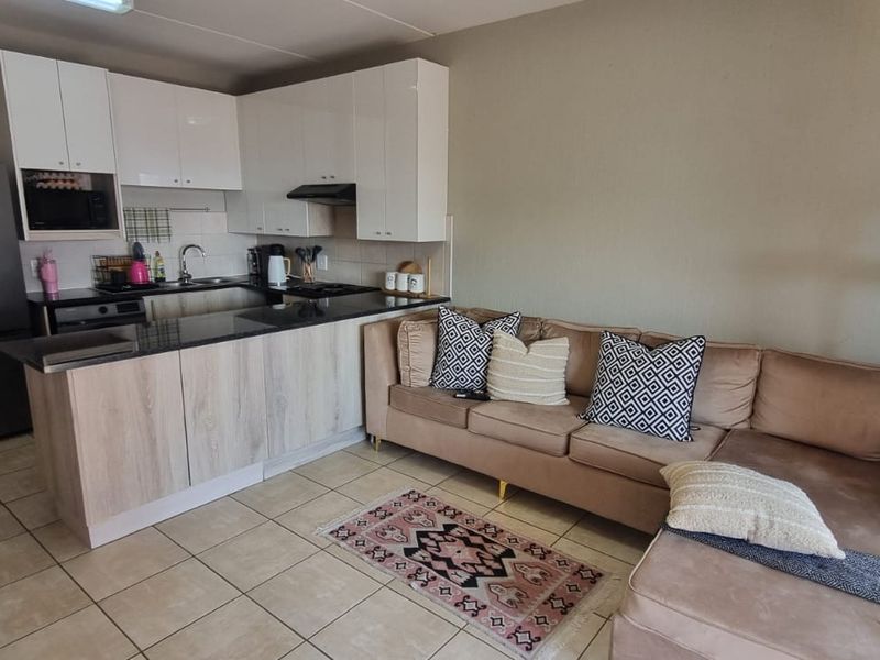 Open plan living area featuring a compact kitchen with modern cabinetry, granite countertops, and tiled flooring, seamlessly integrated with the adjacent lounge space.