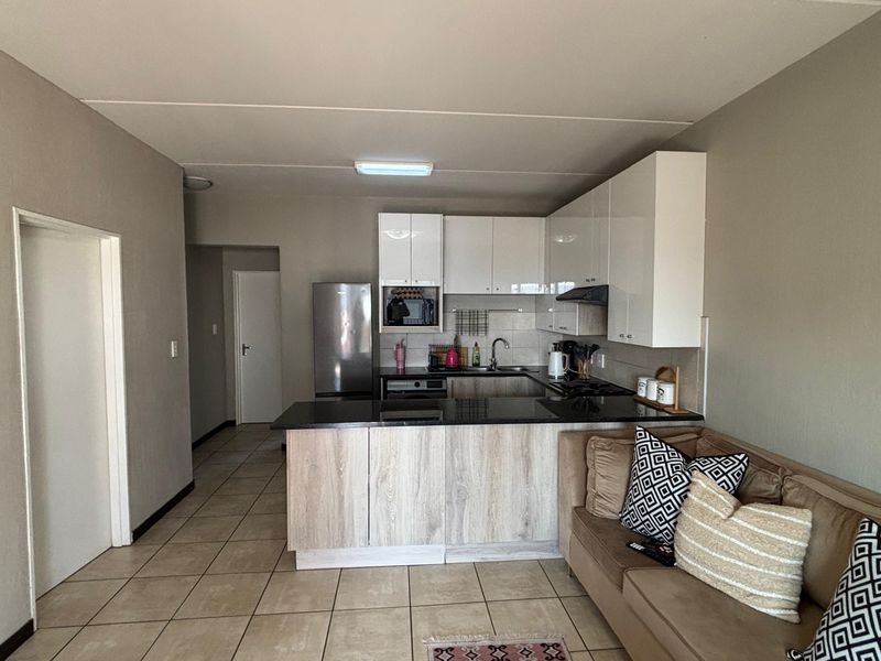 Open-plan kitchen featuring modern white cabinetry, dark laminate countertops, and tiled flooring, seamlessly integrated with the living area.