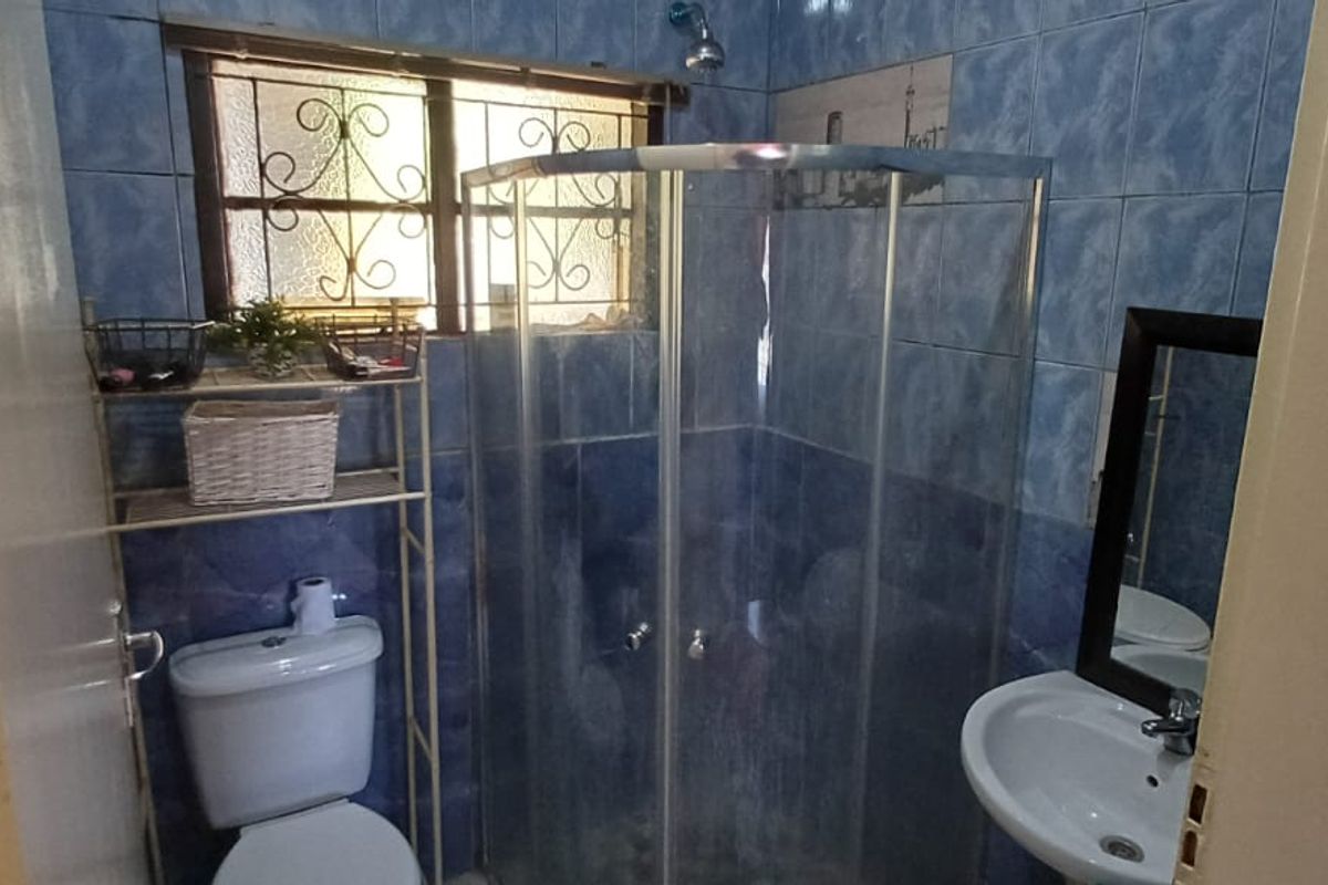 A compact bathroom featuring a corner shower enclosure, a standard toilet, and a wall-mounted basin with blue tiled walls.