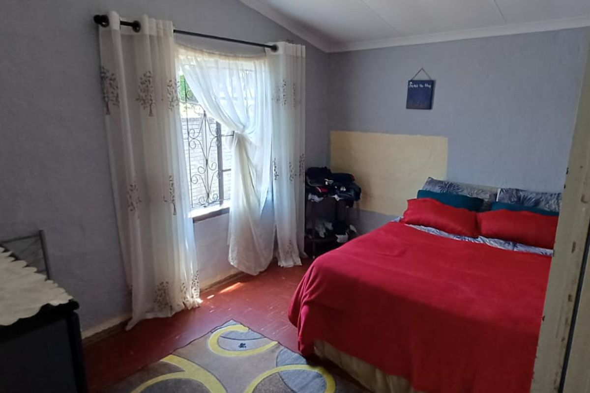 A bedroom featuring a window with security bars, textured walls, and painted flooring.