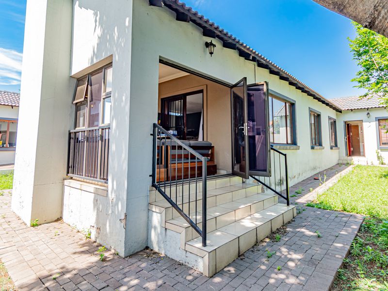 Rear exterior view of the townhouse featuring a paved walkway, tiled patio steps with metal handrails, and access to the interior living space.