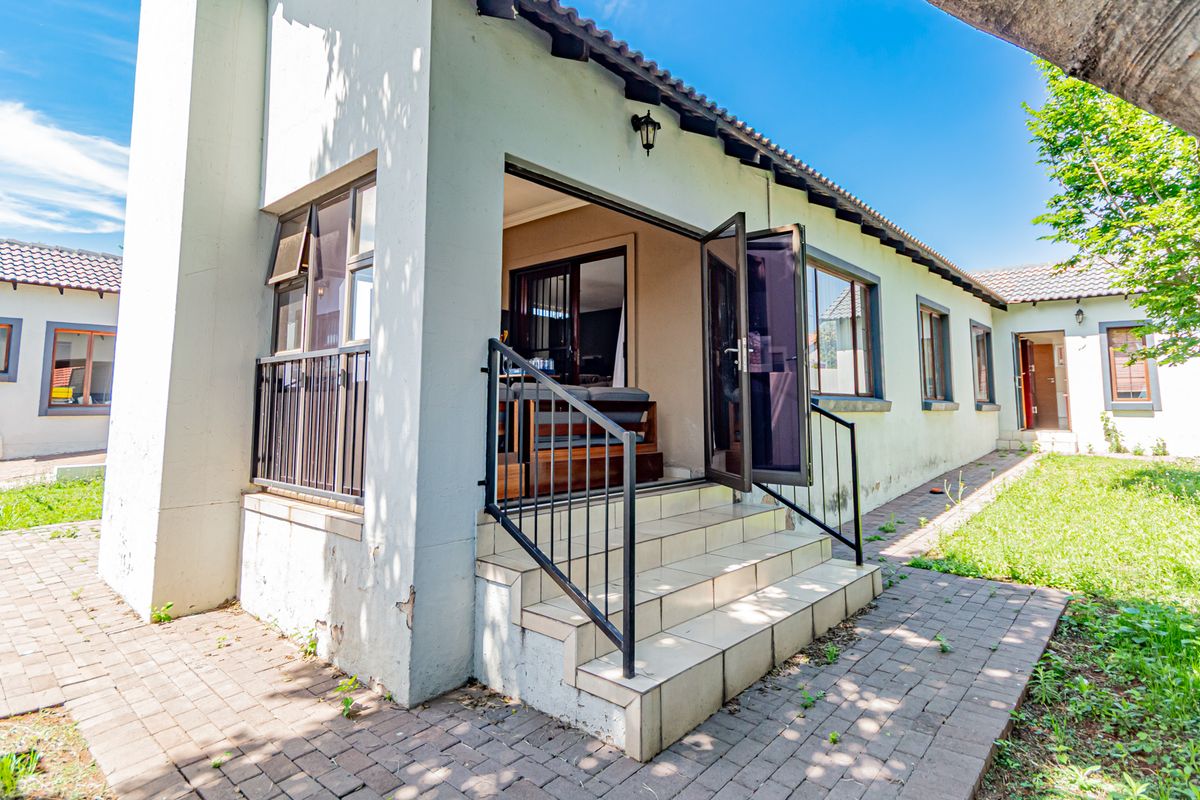 Rear exterior view of the townhouse featuring a paved walkway, tiled patio steps with metal handrails, and access to the interior living space.