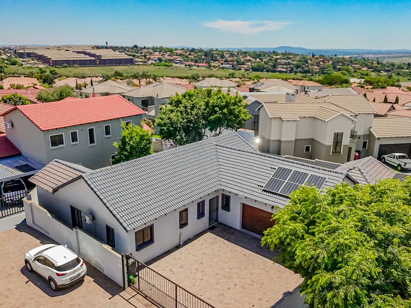 Aerial view of a townhouse property featuring a tiled roof with solar panels, a paved driveway, and secure perimeter fencing within a residential estate.