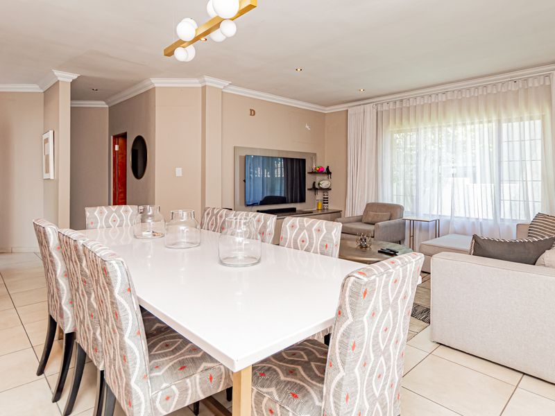 Spacious open-plan living and dining area featuring tiled floors, crown molding, recessed lighting, and a built-in media unit, offering a bright and functional layout.