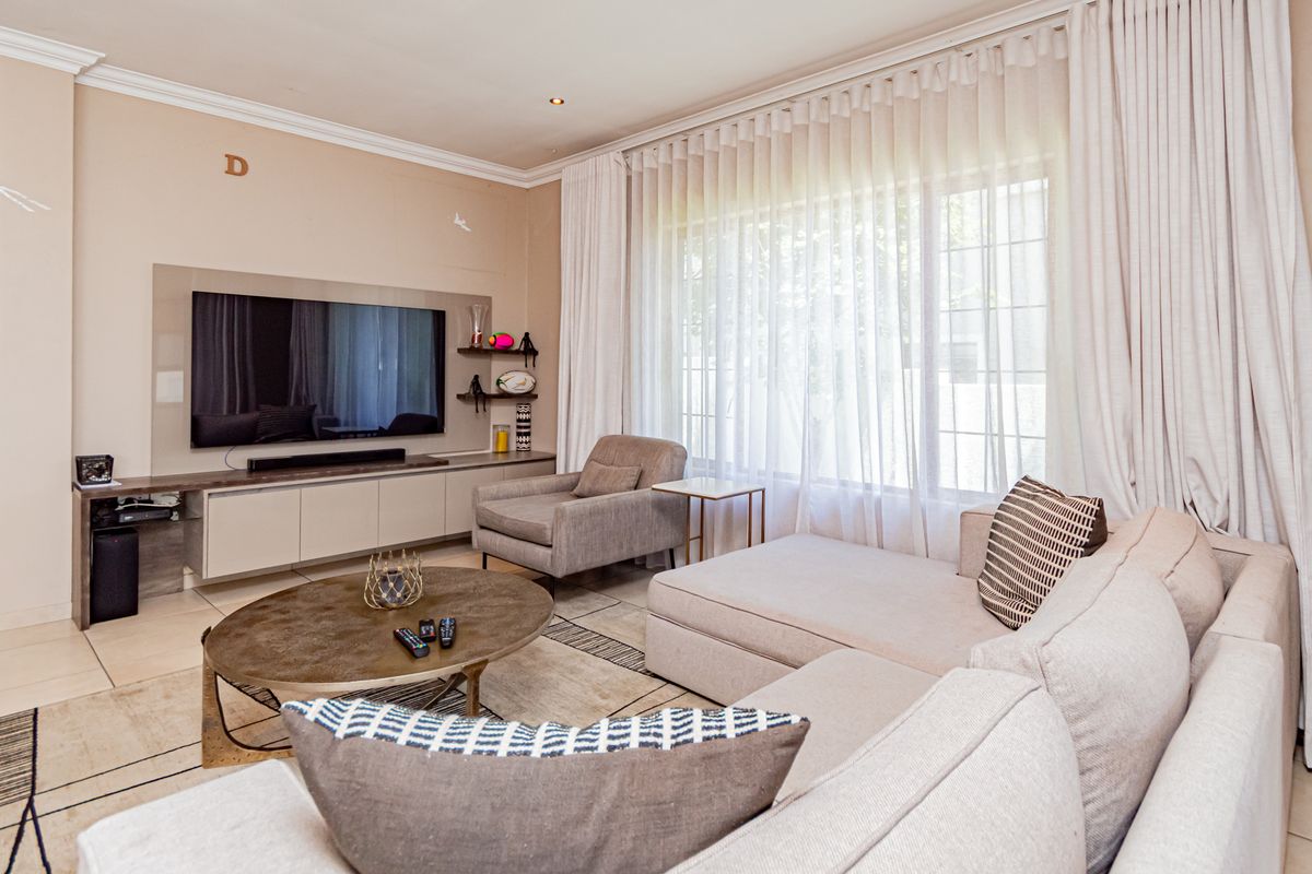 A well-maintained living room featuring built-in cabinetry, recessed downlights, crown molding, and large windows with floor-to-ceiling curtains.