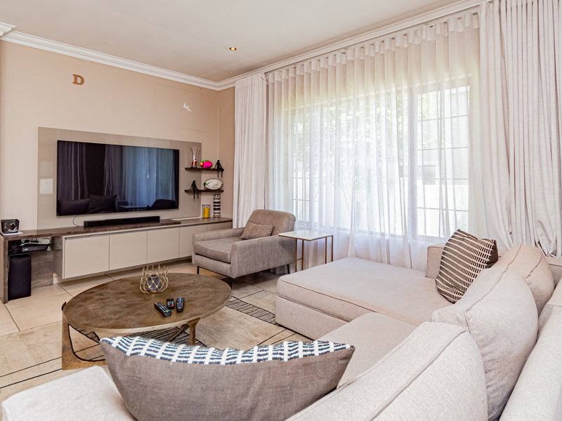 A well-maintained living room featuring built-in cabinetry, recessed downlights, crown molding, and large windows with floor-to-ceiling curtains.
