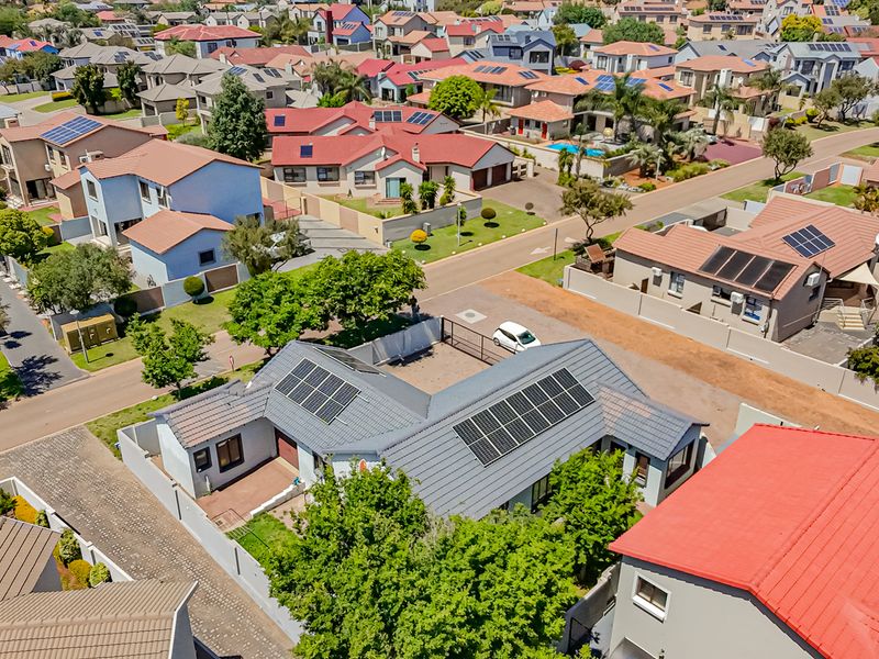Aerial view of the townhouse property featuring a tiled roof with installed solar panels, a paved driveway, and secure boundary walls within a residential estate.