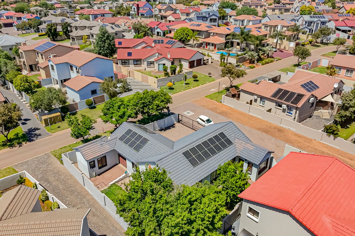 Aerial view of the townhouse property featuring a tiled roof with installed solar panels, a paved driveway, and secure boundary walls within a residential estate.