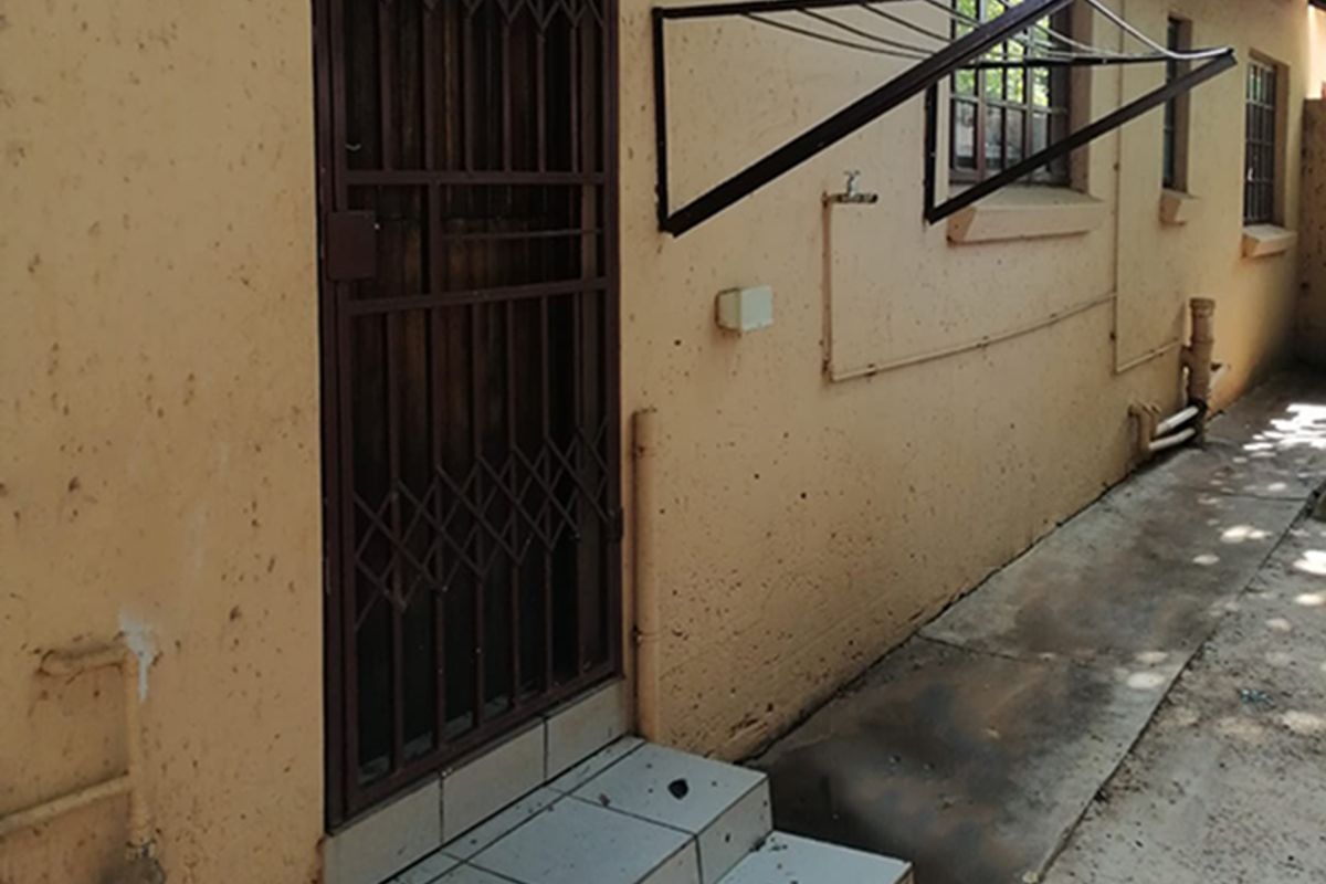 Exterior view of the rear townhouse area featuring a security gate, tiled step, wall-mounted drying rack, and external plumbing fixtures.