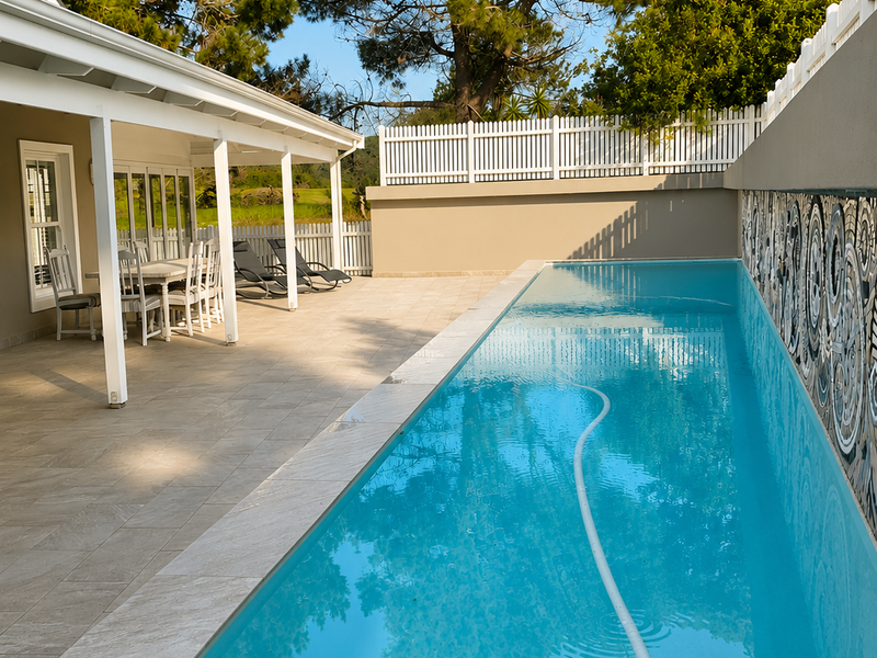 A well-maintained swimming pool area featuring a covered patio, decorative tiled feature wall, and clean paved surrounds, perfect for outdoor relaxation.