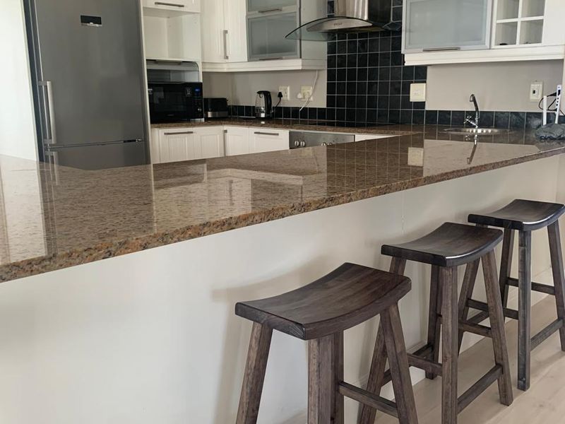 A functional kitchen featuring granite countertops, a stainless steel extractor fan, tiled backsplash, and ample built-in cabinetry with a breakfast bar.