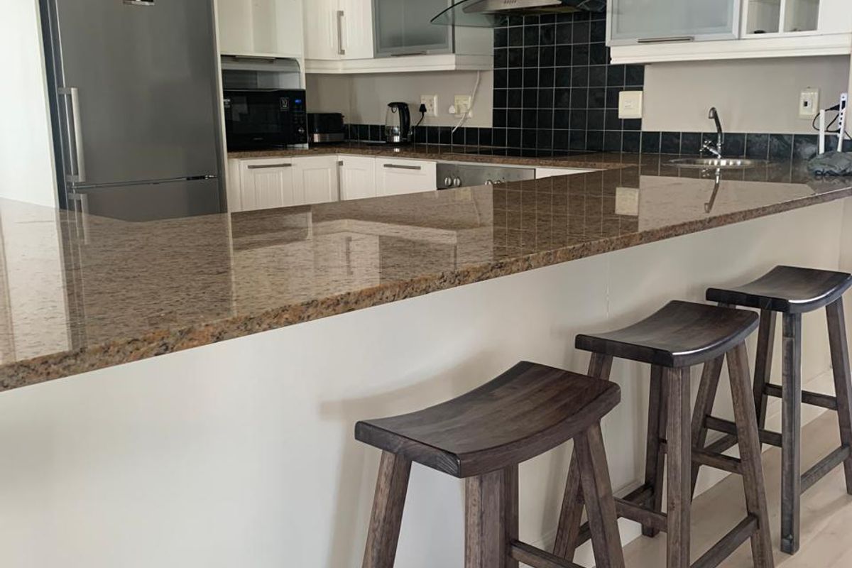 A functional kitchen featuring granite countertops, a stainless steel extractor fan, tiled backsplash, and ample built-in cabinetry with a breakfast bar.