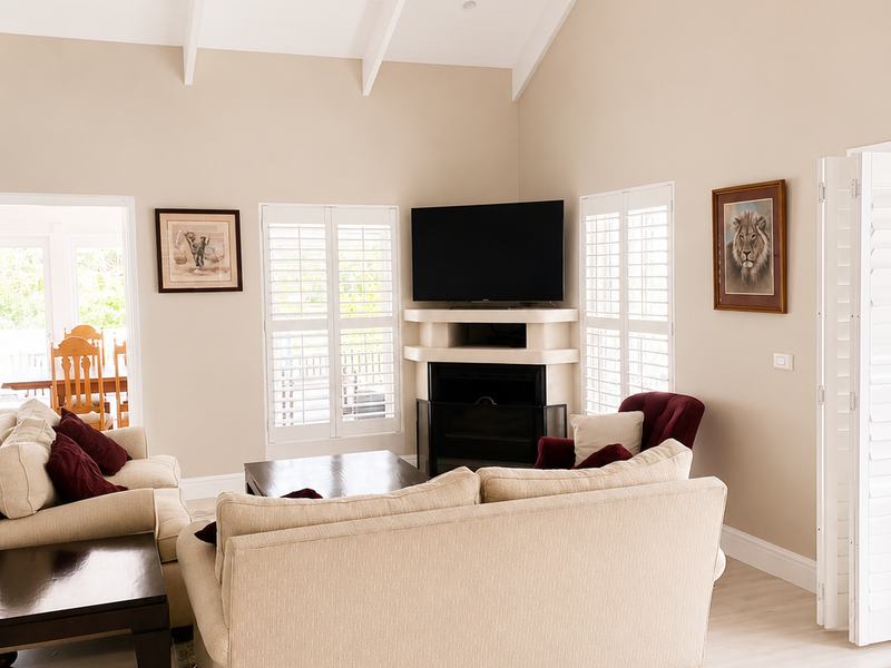 Spacious living room featuring a high vaulted ceiling with exposed beams, a corner fireplace, and plantation shutters allowing for ample natural light.