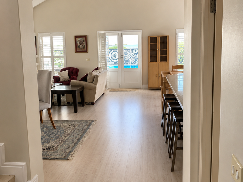 Spacious open-plan living area featuring light laminate flooring, vaulted ceilings, and double french doors leading to an outdoor pool area.