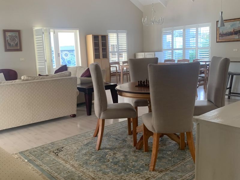 Spacious open-plan living and dining area featuring high vaulted ceilings with exposed beams, light laminate flooring, and plantation shutters.