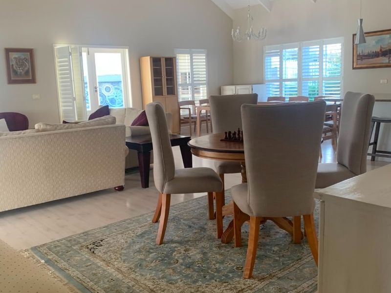 Spacious open-plan living and dining area featuring high vaulted ceilings with exposed beams, light laminate flooring, and plantation shutters for natural light control.