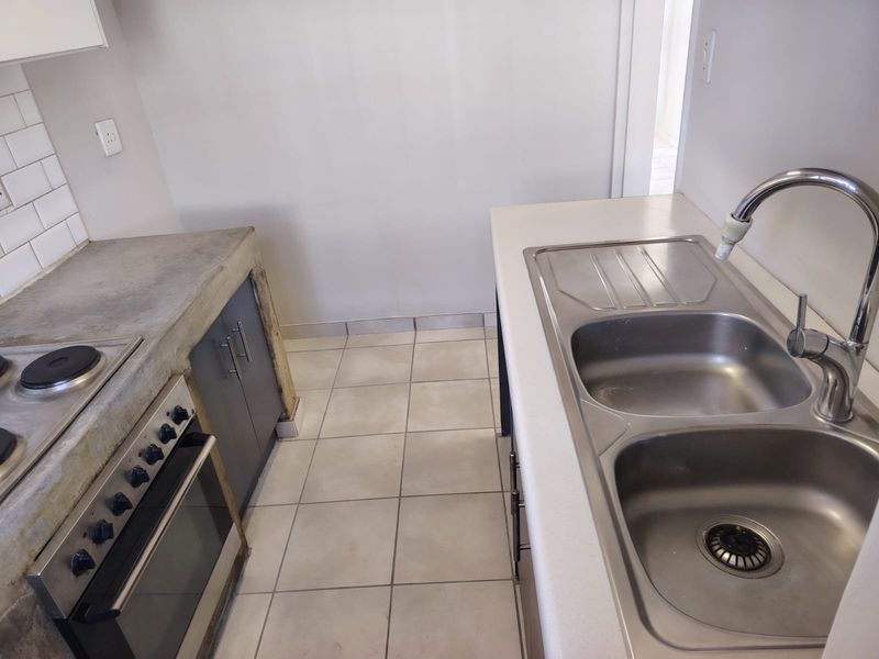 A functional kitchen featuring a built-in oven, electric hob, double stainless steel sink, and tiled flooring with a subway tile backsplash.