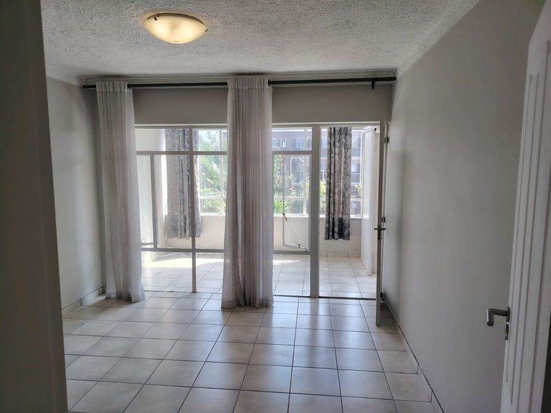 An empty living room featuring tiled flooring and large glass sliding doors that open onto an adjacent patio area.