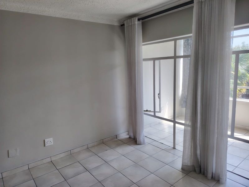 An empty living room featuring tiled flooring and a large glass sliding door leading to an outdoor area, offering a bright and neutral space.