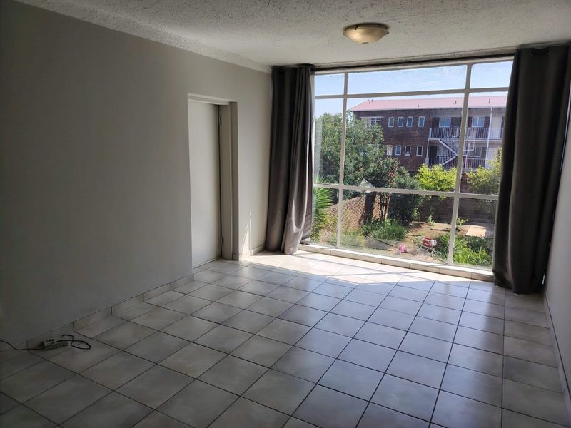 An empty living room featuring large floor-to-ceiling windows that provide natural light and a view of the garden area.
