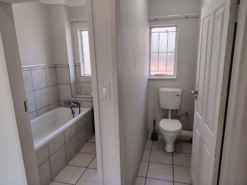 A functional bathroom featuring a separate bathtub area and a private toilet, finished with neutral floor and wall tiling.