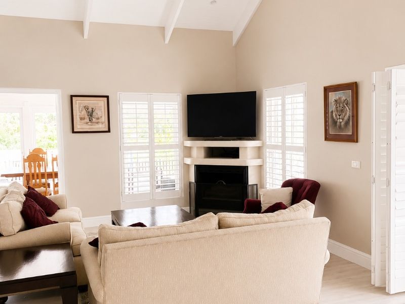 Spacious living room featuring a high vaulted ceiling with exposed beams, a corner fireplace, and plantation shutters, creating a bright and inviting atmosphere.
