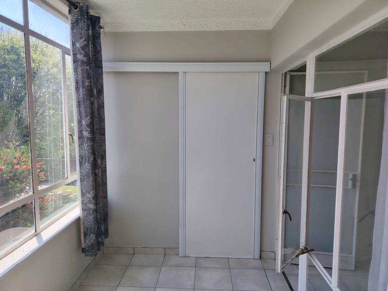 A bright, enclosed patio or sunroom featuring tiled flooring, a large window, and a sliding door, offering a versatile space with natural light.