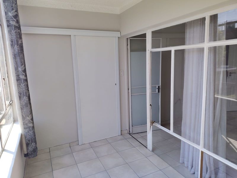An enclosed patio or sunroom featuring tiled flooring, a built-in cupboard, and a glass partition wall leading to an adjacent space.